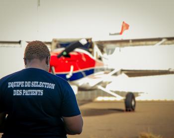 Mercy Ships patient selection staff member stands in front of MAF plane